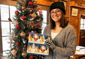 A woman smiling next to a Christmas tree at Stone Mill Clothing & Gifts in Lanesboro, MN